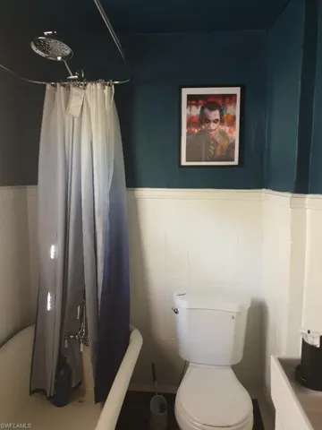 Full bathroom with toilet, curtained shower, tile walls, and wainscoting