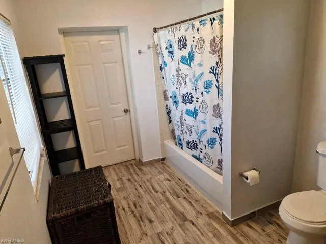 Bathroom with shower / tub combo, baseboards, toilet, and wood finished floors