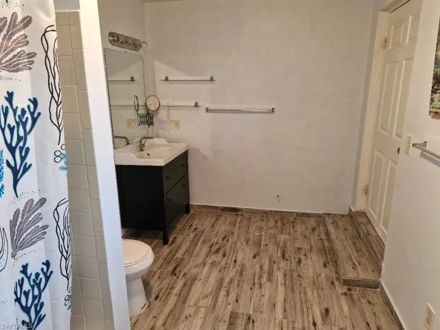 Bathroom featuring toilet, vanity, wood finished floors, a shower with curtain, and baseboards