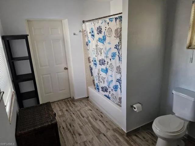 Bathroom with toilet, shower / bath combo, baseboards, and wood finished floors