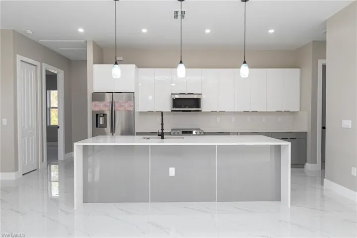 Kitchen with appliances with stainless steel finishes, white cabinets, and a center island with sink