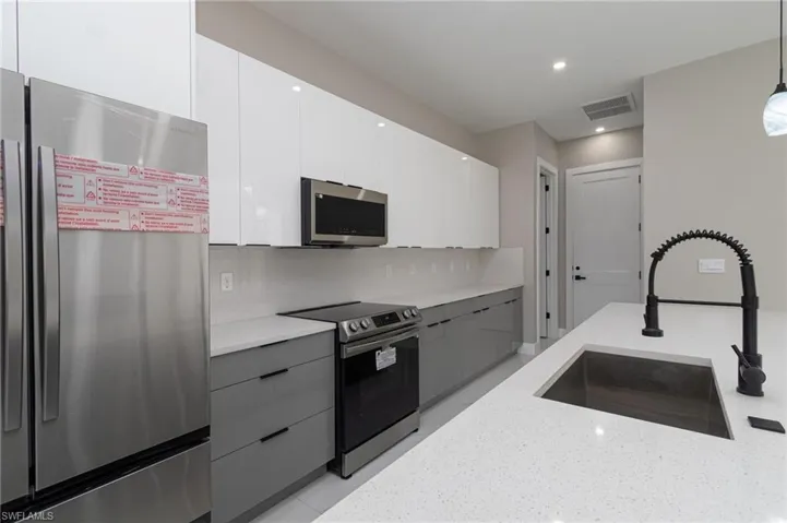 Kitchen featuring stainless steel appliances, sink, decorative light fixtures, white cabinets, and light stone counters