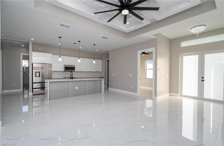 Kitchen featuring white cabinets, hanging light fixtures, a raised ceiling, a kitchen island with sink, and stainless steel appliances