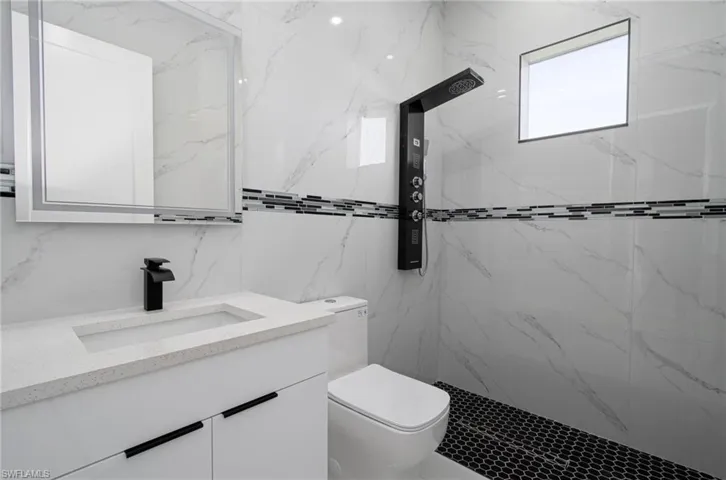 Bathroom with a tile shower, backsplash, toilet, tile walls, and vanity