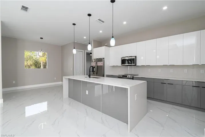 Kitchen with an island with sink, stainless steel appliances, sink, pendant lighting, and white cabinets