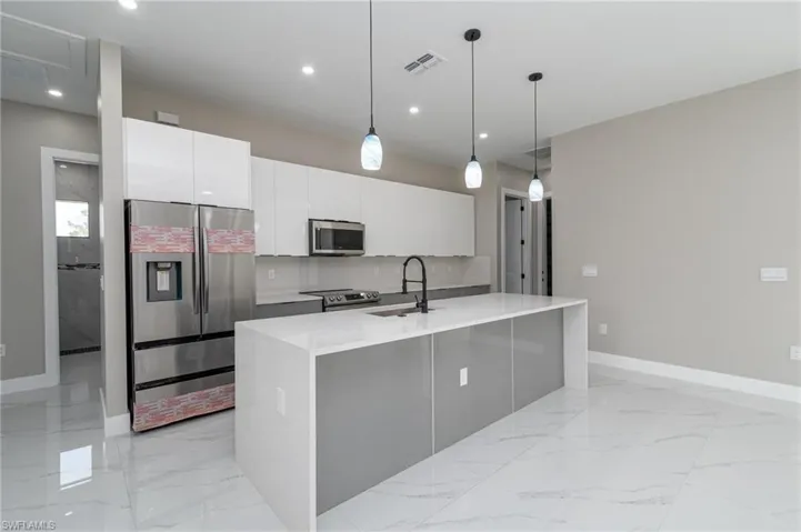 Kitchen featuring white cabinets, hanging light fixtures, a center island with sink, sink, and stainless steel appliances