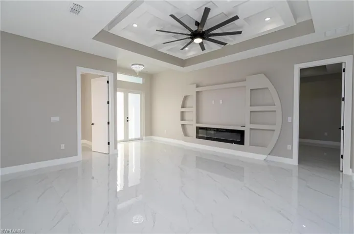 Unfurnished living room featuring french doors, ceiling fan, and a tray ceiling
