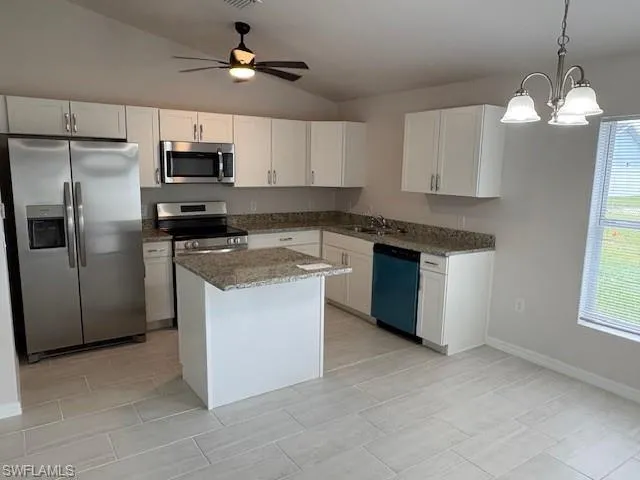 Kitchen with a center island, stainless steel appliances, lofted ceiling, decorative light fixtures, and white cabinets