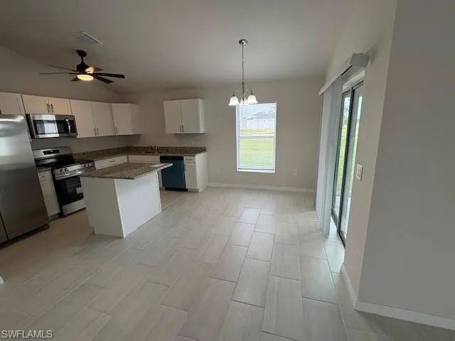 Kitchen with white cabinets, ceiling fan with notable chandelier, hanging light fixtures, appliances with stainless steel finishes, and a kitchen island