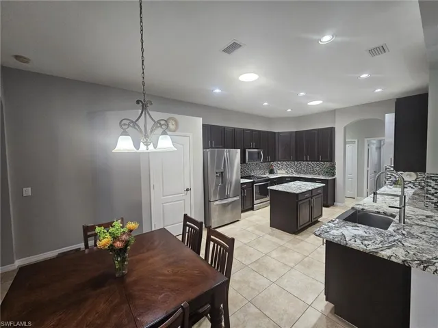 Kitchen featuring dark wood cabinetry, stainless steel appliances, a center island, granite countertops, and a patterned tile backsplash