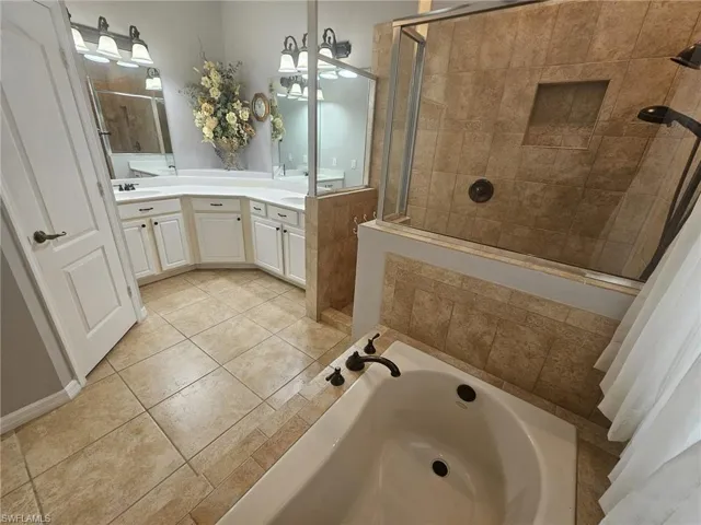 Bathroom featuring a built-in bathtub, a walk-in shower with glass enclosure, dual vanity sinks, and tile flooring