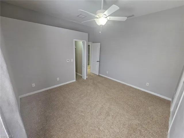 Neutral gray wall paint with white trim, tan carpet flooring, and a ceiling fan with integrated lighting