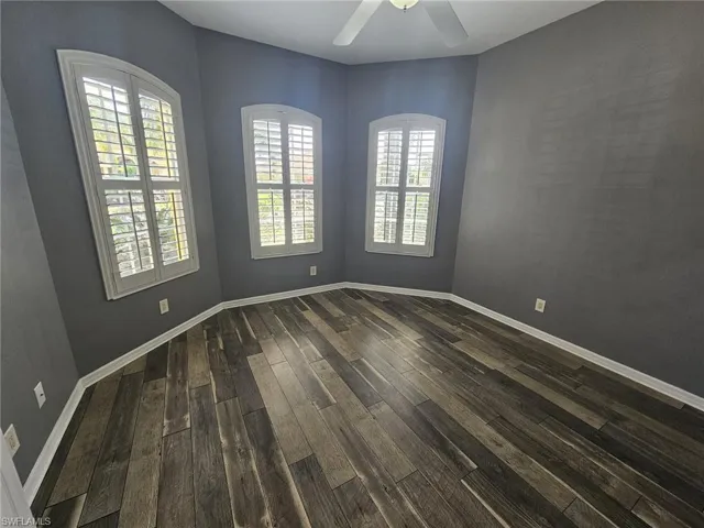 Room featuring three arched windows with plantation shutters, wood-finish flooring, and a ceiling fan