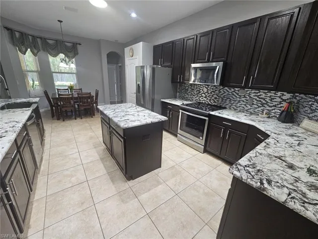 Spacious kitchen featuring dark wood cabinetry, light-toned tiled flooring, and a central island with a light-colored countertop