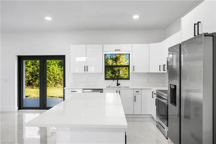 Kitchen with light tile flooring, sink, electric range oven, white cabinets, and stainless steel fridge with ice dispenser
