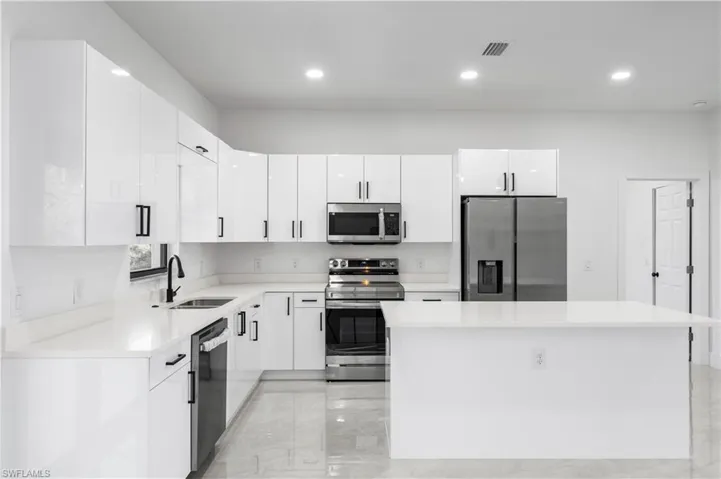 Kitchen featuring a kitchen island, light tile floors, sink, white cabinetry, and appliances with stainless steel finishes