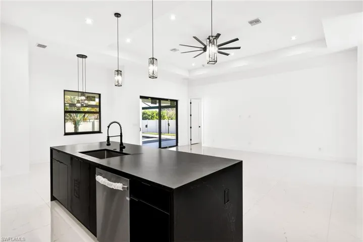 Kitchen with dark cabinets, decorative light fixtures, an island with sink, dishwasher, and a tray ceiling