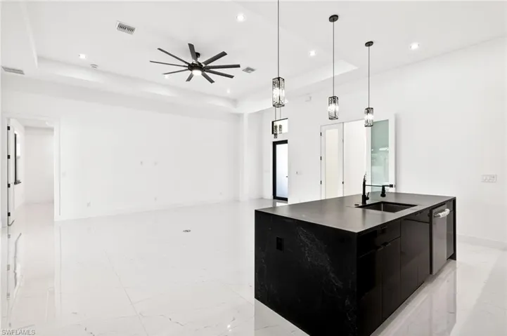 Kitchen featuring dark cabinetry, hanging light fixtures, a kitchen island with sink, a tray ceiling, and light marble finish flooring