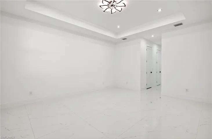 Spare room with a tray ceiling, recessed lighting, and light marble finish flooring