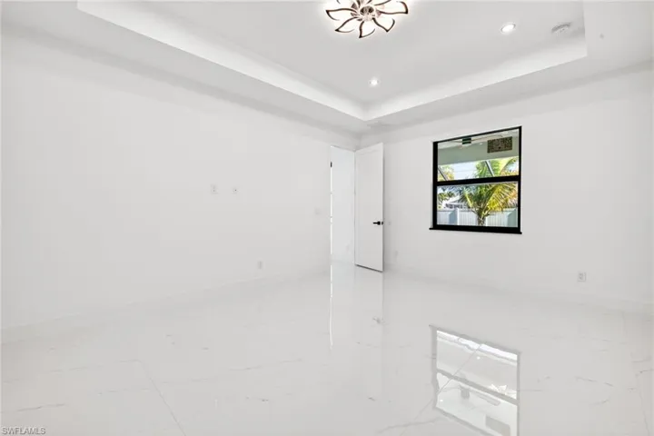 Empty room featuring a raised ceiling, recessed lighting, and light marble finish flooring