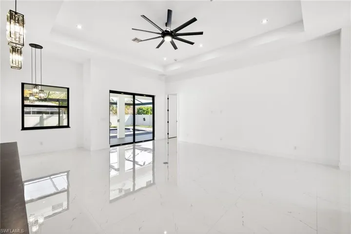 Spare room featuring a tray ceiling, light marble finish flooring, a ceiling fan, and hanging lights