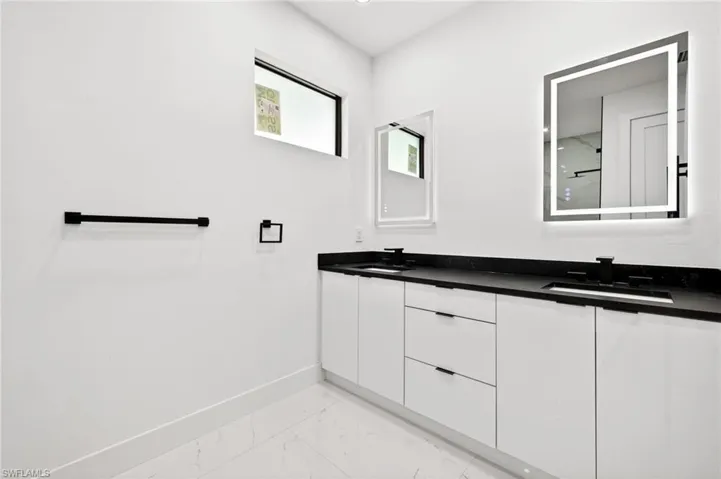 Full bathroom featuring double vanity, light marble finish floors, and a shower