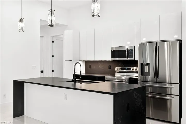 Kitchen with stainless steel appliances, an island with sink, modern cabinets, decorative light fixtures, and white cabinetry
