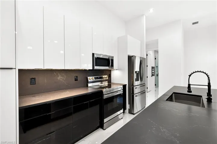 Two tone kitchen featuring modern cabinets, stainless steel appliances, backsplash, recessed lighting, and dual tone cabinets