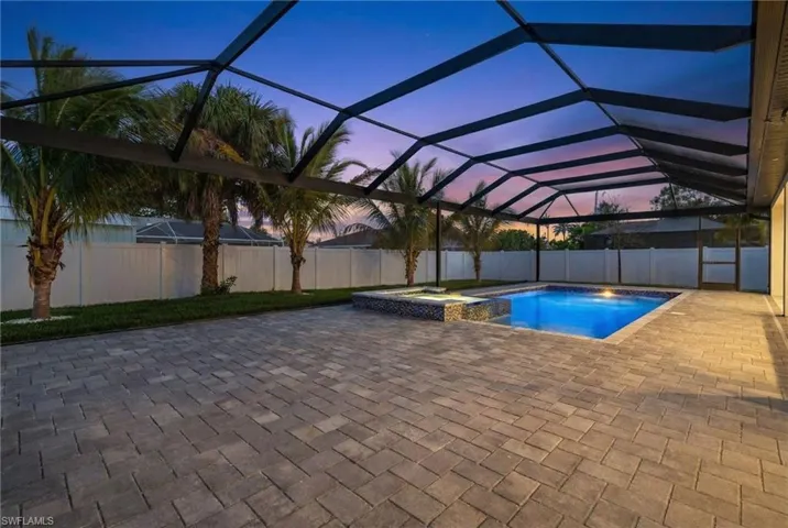 Pool at dusk with glass enclosure, a fenced backyard, a sunroom, a pool with connected hot tub, and a patio