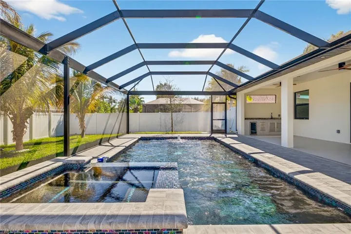 Integrated pool / hot tub featuring a sunroom, an outdoor kitchen, a patio area, and glass enclosure