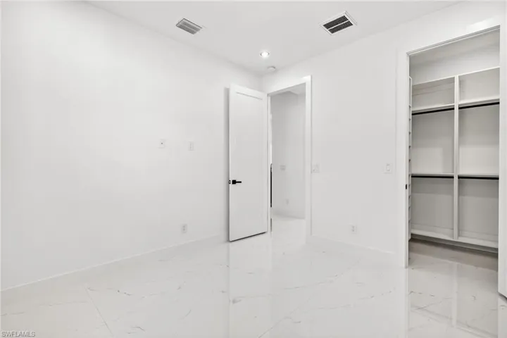 Unfurnished bedroom featuring light marble finish floors, a walk in closet, and recessed lighting
