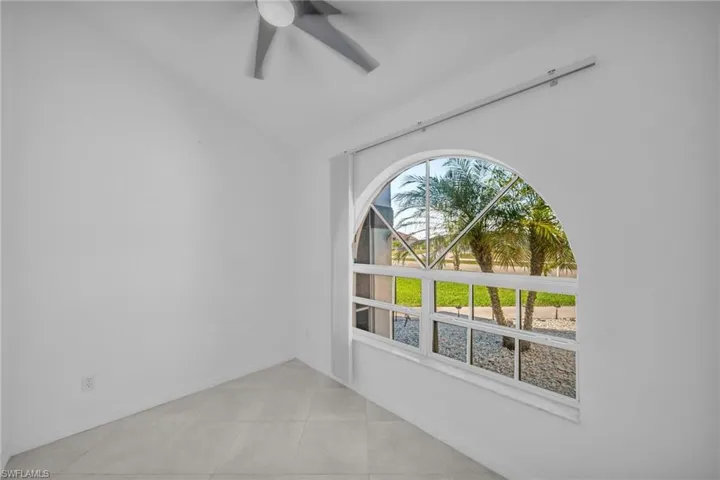 Empty room with a ceiling fan, lofted ceiling, and light tile patterned floors