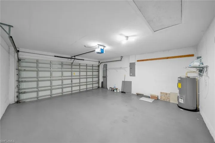 Garage featuring electric panel, electric water heater, and a garage door opener