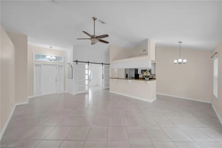 Unfurnished living room with hanging lights, a barn door, ceiling fan, vaulted ceiling, and light tile patterned floors