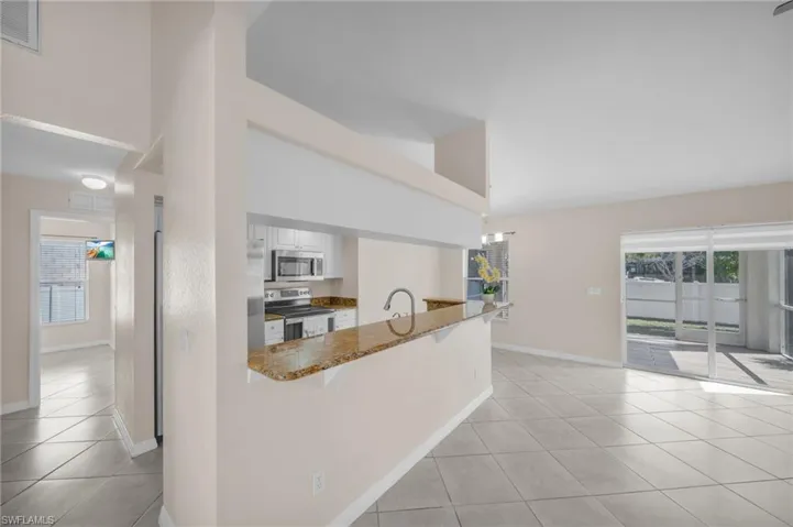 Kitchen featuring stainless steel appliances, dark stone counters, a breakfast bar area, white cabinetry, and light tile patterned flooring