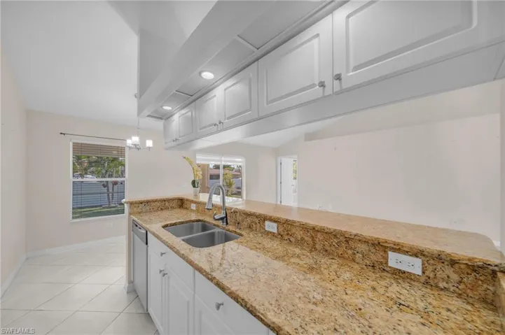 Kitchen featuring light stone countertops, white cabinetry, hanging light fixtures, and plenty of natural light