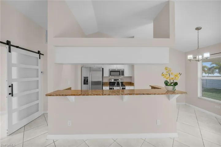 Kitchen featuring a barn door, a kitchen breakfast bar, dark stone countertops, stainless steel appliances, and lofted ceiling