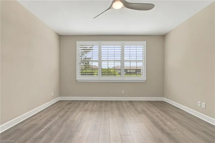 Wood-finish flooring, neutral wall tones, window with plantation shutters, ceiling fan with integrated lighting