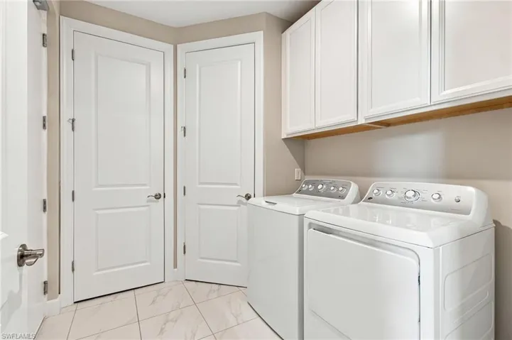 Laundry area featuring overhead white shaker-style cabinetry, a wood-finish shelf, and white tile flooring