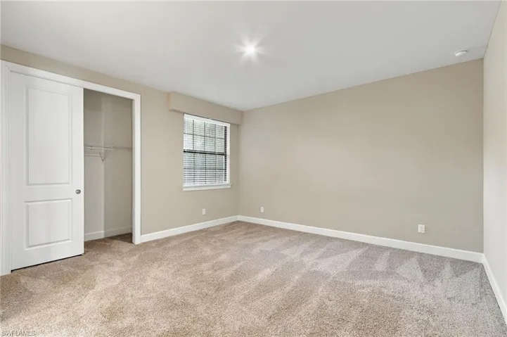 Expansive carpeted flooring, neutral wall tones, window with horizontal blinds, built-in closet with shelving, and recessed ceiling lighting