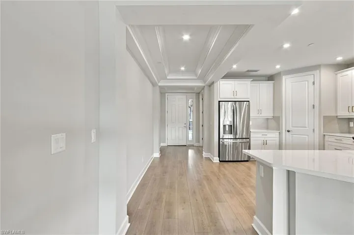 Wood-finish flooring, recessed lighting, coffered ceiling detail, stainless steel refrigerator, and white kitchen cabinetry with a light-toned countertop