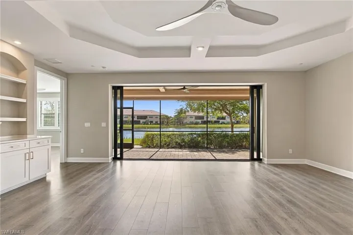 Wood-finish flooring, tray ceiling, built-in cabinetry with open shelving, and a screened patio with water scenery