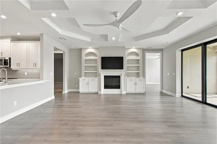 Tray ceiling with recessed lighting and a ceiling fan, wood-finish flooring, built-in shelving and cabinetry flanking a fireplace, and large sliding glass doors