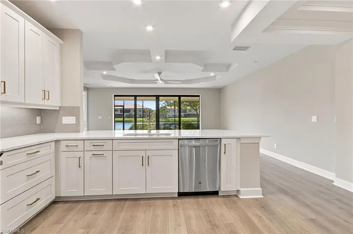 Modern kitchen featuring white shaker cabinetry, quartz countertops, a herringbone tile backsplash, wood-finish flooring, and a stainless steel dishwasher