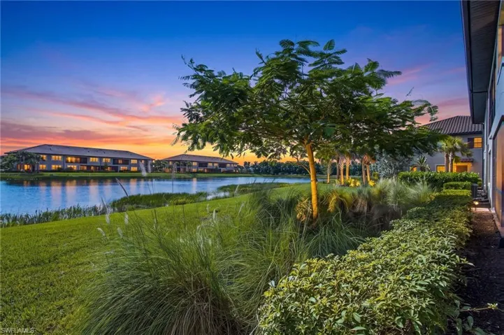 Manicured landscaping with mature trees, green lawn, and a water feature bordering the property