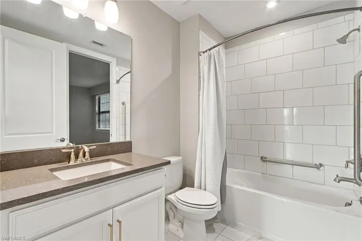 White subway tile shower surround with grab bars, single vanity with light-colored countertop and undermount sink, and recessed lighting