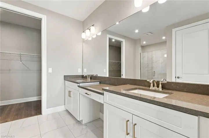 White shaker-style cabinetry with gold-finish hardware, dual undermount sinks, stone countertops, and a full-width vanity mirror