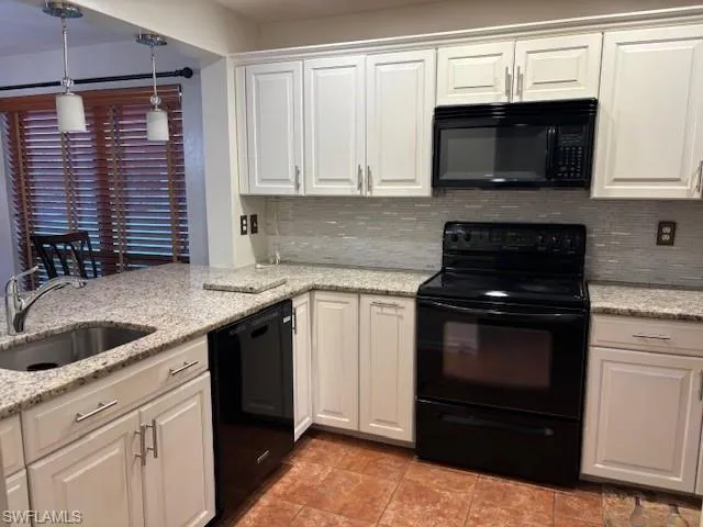 Kitchen with black appliances, white cabinetry, light stone counters, tasteful backsplash, and pendant lighting