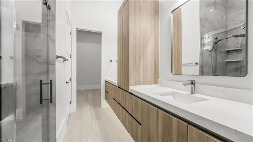 Bathroom featuring double vanity, a marble finish shower, and light wood-type flooring