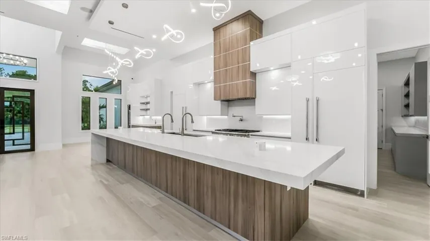 Kitchen featuring modern cabinets, a large island, brown cabinets, white cabinetry, and a high ceiling